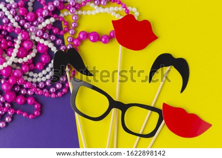 Party kit for Mardi Gras carnival (birthday, corporate celebration, wedding) and beads on yellow and purple paper background. Flat lay