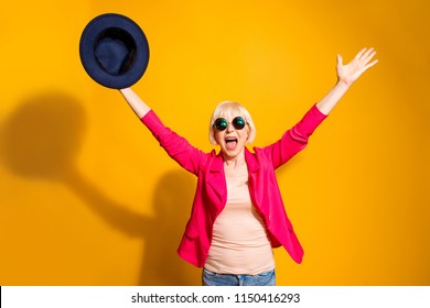 Party Mood! Portrait Of Old Woman Stretching Her Arms Upwards Waving Her Hat Celebrating The Victory Isolated On Vivid Yellow Background