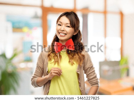 party props and people concept - happy asian young woman with big red bow tie over office background