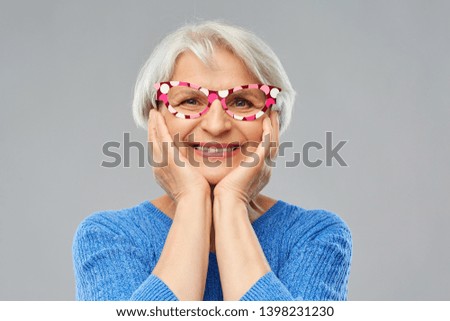 party props, photo booth and old people concept - portrait of amazed smiling senior woman in blue sweater with big glasses over grey background