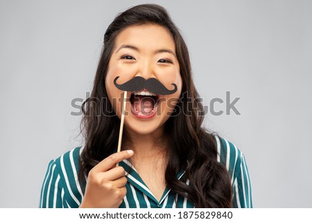 party props, photo booth and people concept - happy asian young woman with big black moustaches over grey background