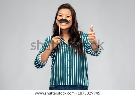 party props, photo booth and people concept - happy asian young woman with big black moustaches showing thumbs up over grey background