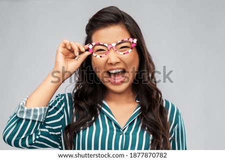 party props, photo booth and people concept - happy asian young woman with glasses over grey background