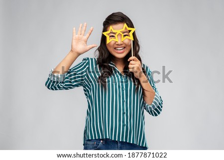 party props, photo booth and people concept - happy asian young woman with big glasses in shape of stars waving hand over grey background