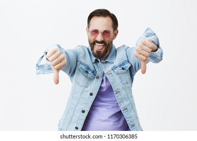 Party Sucks, Go Home. Rebellious Excited Man Being Displeased And Unimpressed, Standing In Sunglasses And Denim Jacket, Showing Thumbs Down And Sticking Tongue Out From Dislike, Negative Feedback