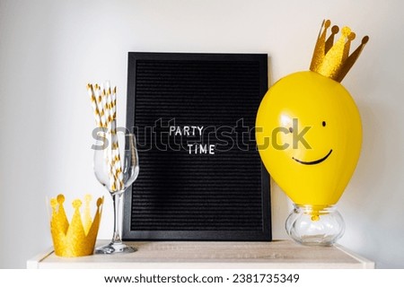 Party time fun celebration event minimal concept with smiling yellow balloon with golden crown, blackboard with text Party time and party stuff on white