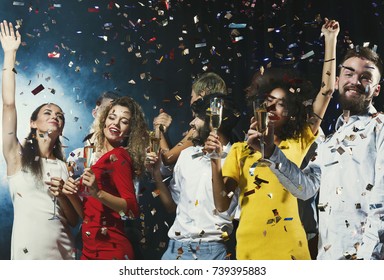 Party time! Happy young people celebrating new year with champagne, having fun and dancing at dark smoky background. Christmas postcard mockup Stockfoto
