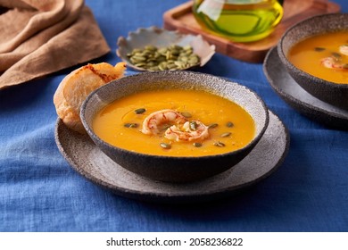 Pascetarian Autumn Homemade Pumpkin And Carrot Cream Puree Soup With Prawn, Seedsand Toast On Plate On Blue Linen Tablecloth. Side View, Close Up, Horizontal. Concept Of Eat Less Meat Food