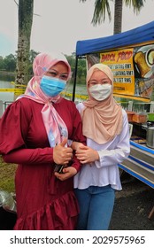 Pasir Gudang, Malaysia - August 24, 2021. Potrait Image Of Two Asian Girl Wearing Face Mask On Hawker Stall And Lake Background.