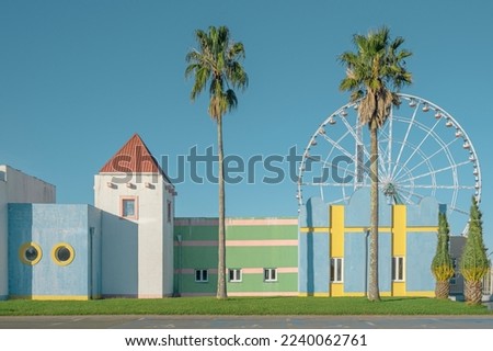 Pasrel colored buildings exterior with palm trees and ferris wheel. Abstract minimal geometric architecture background.