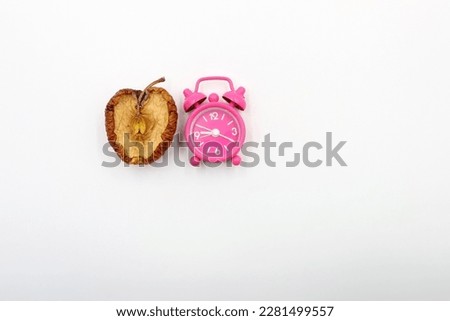 The passage of time. A pink alarm clock next to an aging apple