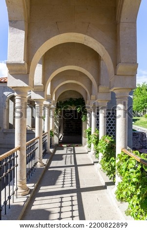 Passageway with white columns in the courtyard of Akhaltsikhe (Rabati) Castle, overgrown by green plants, Georgia.