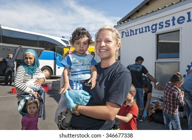 Passau, Germany - August 1, 2015: A German Policewoman Taking Care Of A Young Refugee Child From Syria At The Registration Area In Passau, Bavaria. 