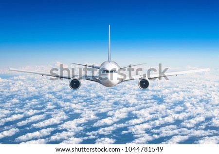 Passenger airplane flying at flight level high in the sky above the clouds and blue sky. View directly in front, exactly.