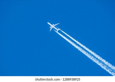 Passenger airplane flying high in clear sky leaving white trails.