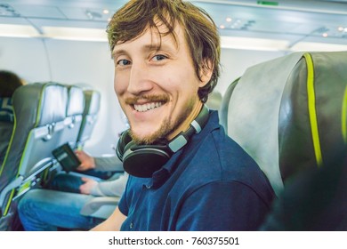 Passenger In Airplane Using Headphones. Man In Plane Cabin Using Smart Device Listening To Music On Headphones.