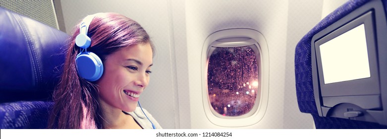 Passenger in airplane using tablet computer. Woman in plane cabin using smart device listening to music on headphones. Banner panorama travel people lifestyle.