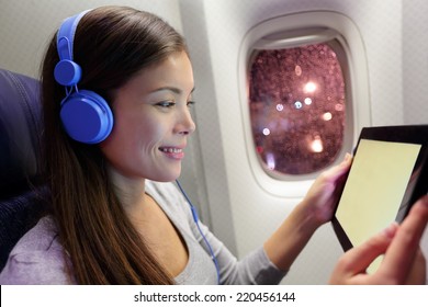 Passenger In Airplane Using Tablet Computer. Woman In Plane Cabin Using Smart Device Listening To Music On Headphones.