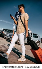 Passenger arrival from travel while pulling red suitcase at the airport and looking at his phone