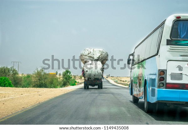 a passenger bus is dangerously overtaking an\
overloaded truck