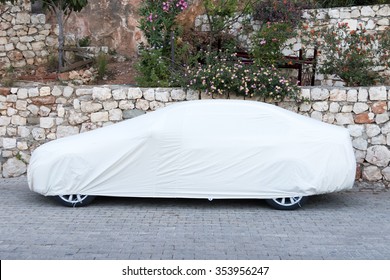 Passenger car covered with white sheet on the pavement
