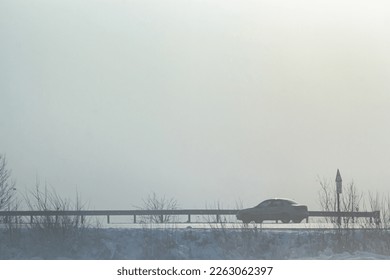 Passenger car in the fog on a winter road with large snowdrifts on the side of the road.