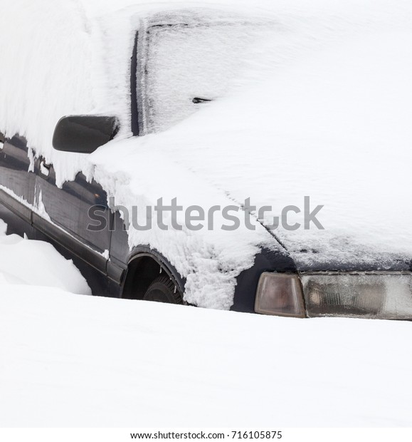 Passenger car in the snowdrift (snow bank) on\
the parking lot. Car covered with snow after the snowstorm in\
winter. Close-up.