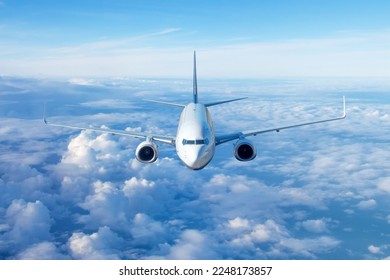 Passenger civil airplane jet flying at flight level high in the sky above the clouds and blue sky. View directly in front, exactly