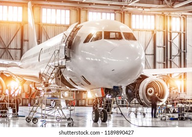 Passenger Commercial Airplane On Maintenance Of Engine Turbo Jet And Fuselage Repair In Airport Hangar. Aircraft With Open Hood On The Nose And Engines, As Well As The Luggage Compartment