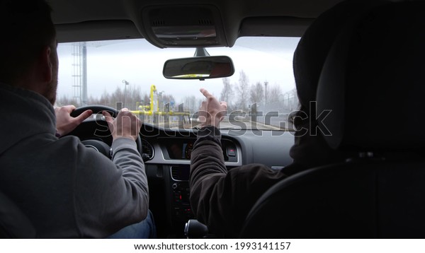 Passenger and driver inside modern car driving\
at industrial site. back view inside car of men pointing outside\
driving in car\
together
