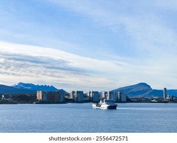 Passenger ferry sailing towards the coastline of a modern city, with snow-capped mountains and cloudy sky in the distance - Powered by Shutterstock