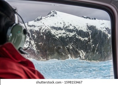 Passenger Of The Helicopter Is Looking On The Glacier From The Window. Amazing Snowy Mountain Peaks. This Is Excursion In Alaska. Sightseeing Tour Over The Glaciers. Blue Ice Field.