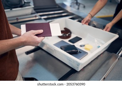 Passenger holding passport against personal Items, liquids, and laptop in container at airport security check. - Shutterstock ID 2053760390
