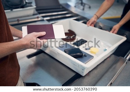 Passenger holding passport against personal Items, liquids, and laptop in container at airport security check.
