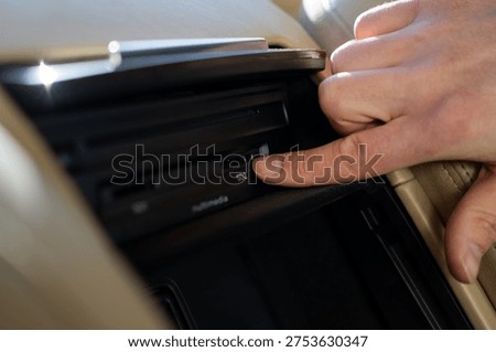 Passenger inserting SD memory card into multimedia slot in the center console of a luxury car.