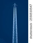 Passenger jet flies overhead with jet stream portrait view with deep blue sky background.