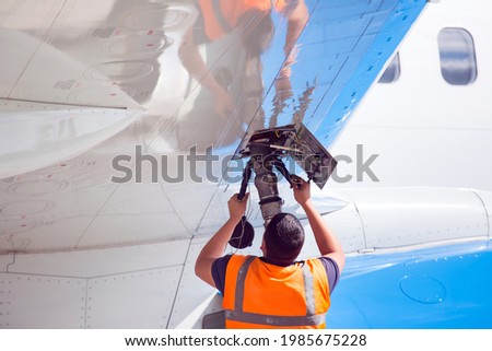 Passenger plane in airport. Technician refueled airplane through the filling valve in the wing.