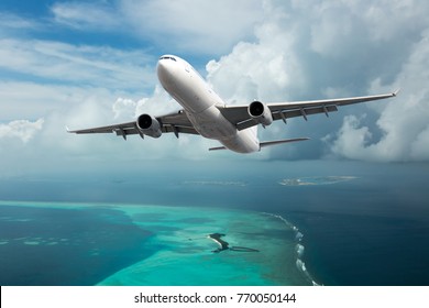 A passenger plane in the cloudy sky. Aircraft flies over the sea and the tropical island. - Shutterstock ID 770050144
