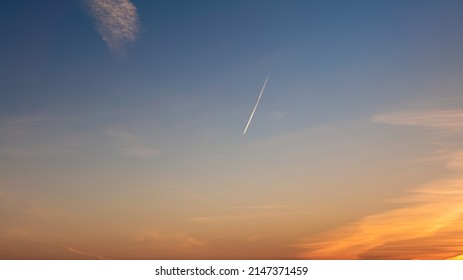 Passenger plane flying in the blue sky at sunset, fast transport leaves behind a white contrail trail. A trace of condensation trails or vapor trails, the aircraft engine exhaust.