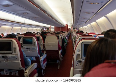 Passenger Seat, Interior Of Airplane With Passengers Sitting On Seats And Stewardess Walking The Aisle In Background