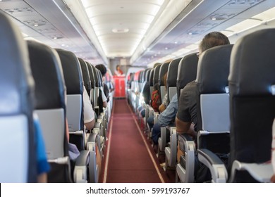 Passenger Seat, Interior Of Airplane With Passengers Sitting On Seats And Stewardess Walking The Aisle In Background. Travel Concept,vintage Color