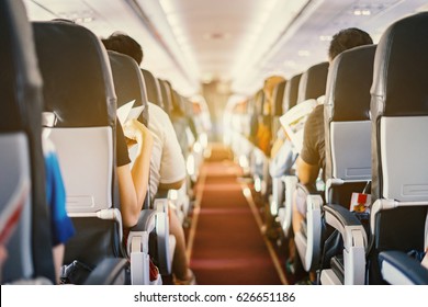 Passenger Seat, Interior Of Airplane With Passengers Sitting On Seats And Stewardess Walking The Aisle In Background. Travel Concept,vintage Color,selective Focus