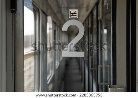 Passenger train corridor glass door with second class number and no smoking symbol sticker. Railroad car interior, inside a train wagon, carriage or compartment coach.