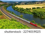 Passenger train rides along the river. Train journey by riverside. River valley train journey. Railroad with train by river