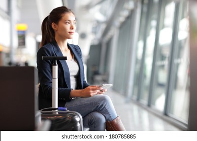 Passenger traveler woman in airport waiting for air travel using tablet smart phone. Young business woman smiling sitting with travel suitcase trolley, in waiting hall of departure lounge in airport.