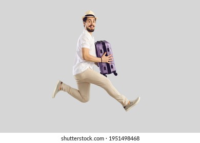 Passenger traveling on weekend, air flight journey concept. Funny cheerful excited man traveler tourist in summer hat jumping hold suitcase luggage. Full length studio portrait on grey copy space