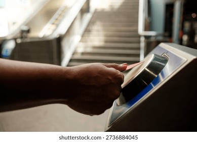 Passenger using electronic ticket validator to enter subway platform, with escalator and stairs in the background, representing urban commuting and access control