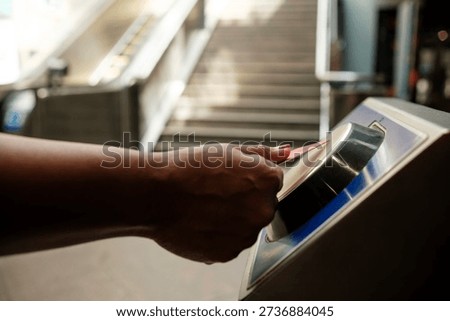 Passenger using electronic ticket validator to enter subway platform, with escalator and stairs in the background, representing urban commuting and access control