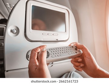 Passenger using remote control to navigate entertainment system during a flight, enjoying movies and music and games
