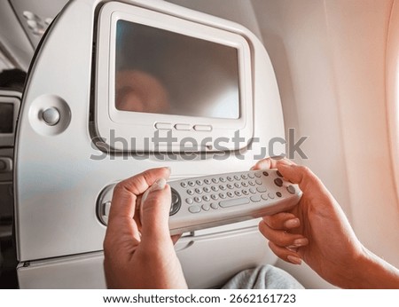 Passenger using remote control to navigate entertainment system during a flight, enjoying movies and music and games